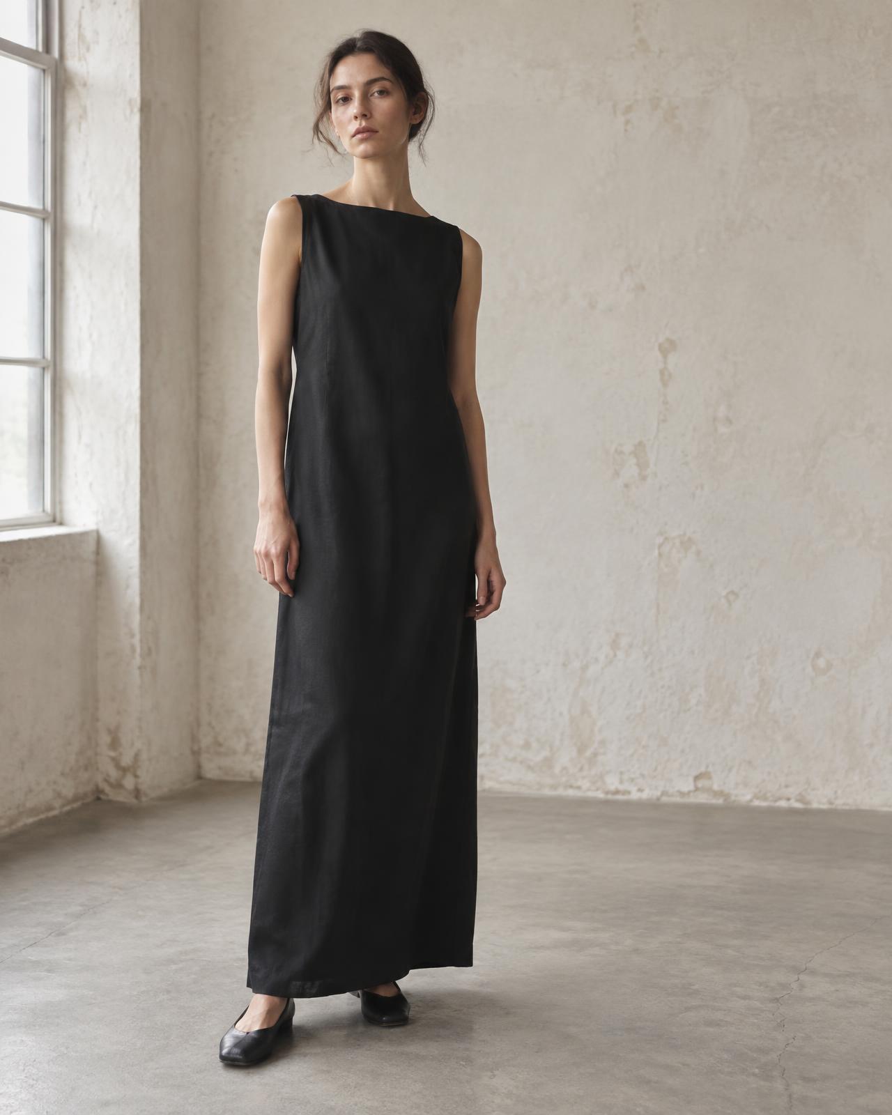 Model wearing the black fluid twill Column Dress in a sunlit atelier